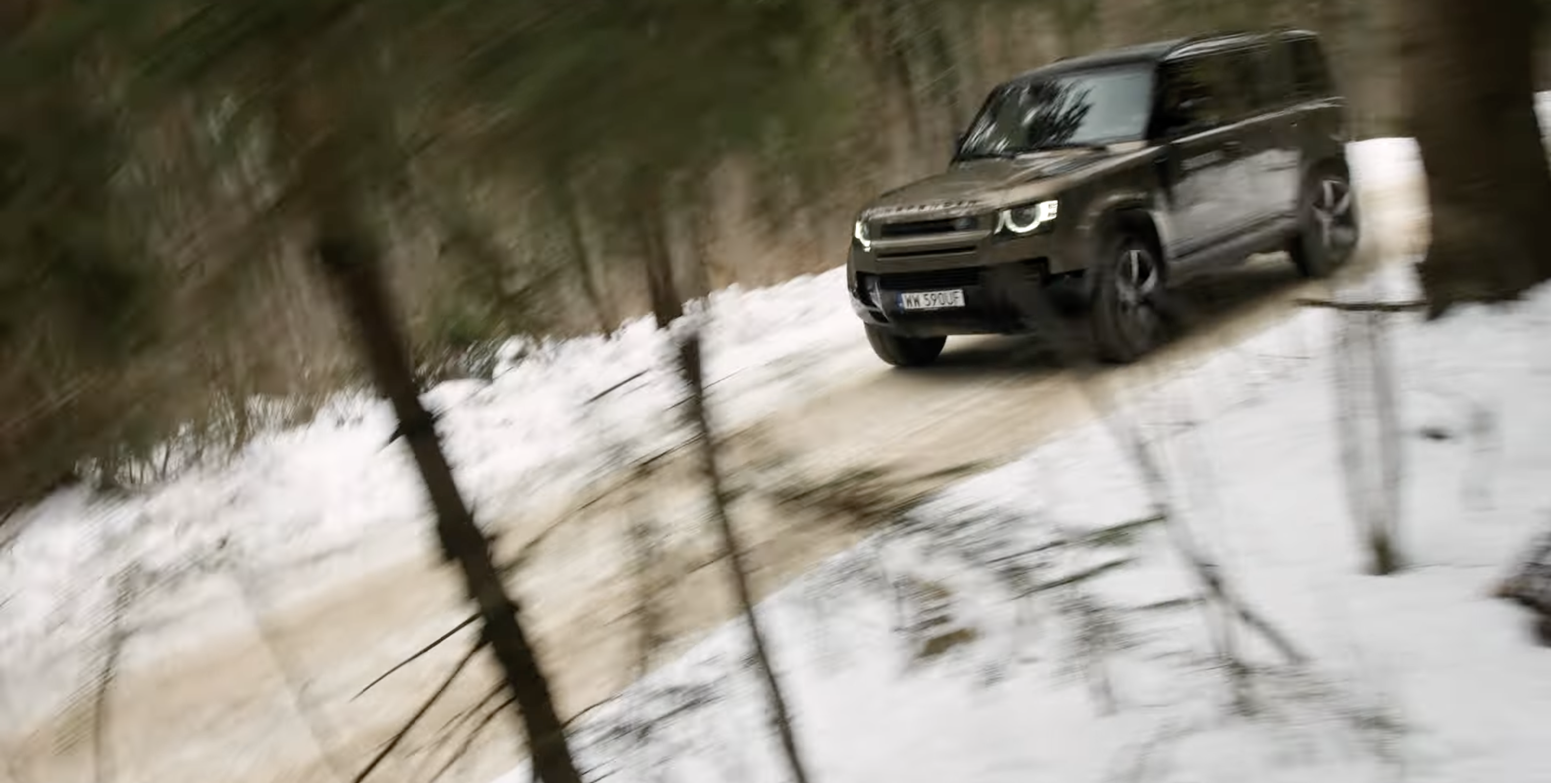 Land Rover Defender jedzie zimową leśną drogą